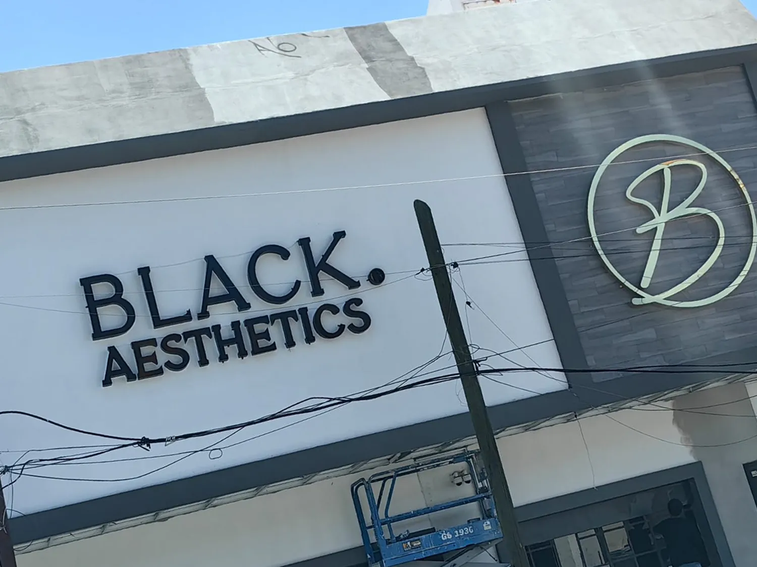 Fachada blanca con letras negras tridimensionales BLACK AESTHETICS y logotipo en neón flex
