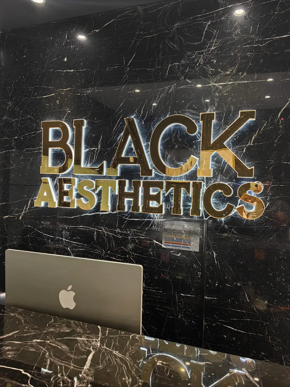 Letras BLACK AESTHETICS en acrílico dorado con luz halo sobre mármol negro