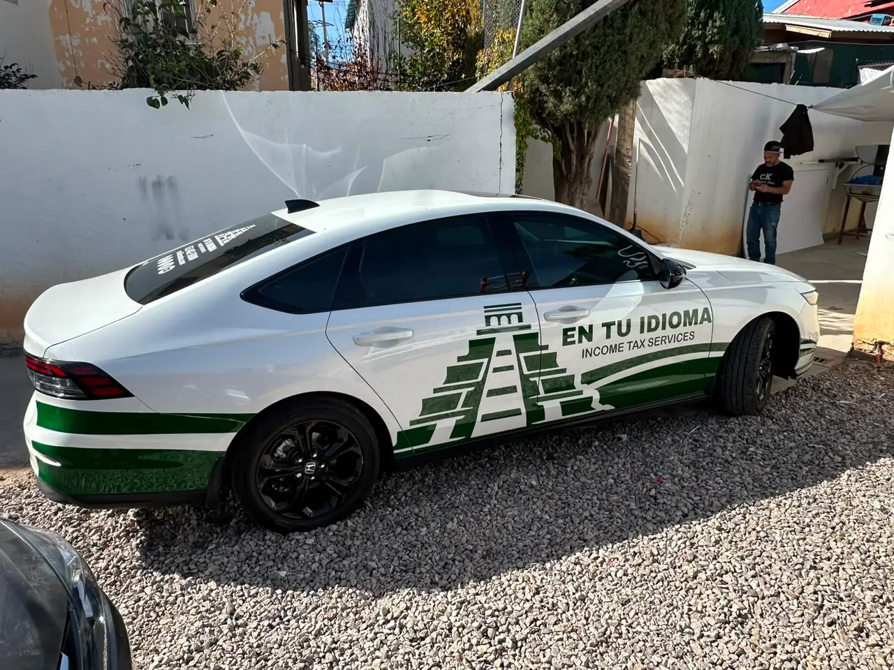 Automóvil blanco rotulado con gráficos verdes y el texto En Tu Idioma Income Tax Services