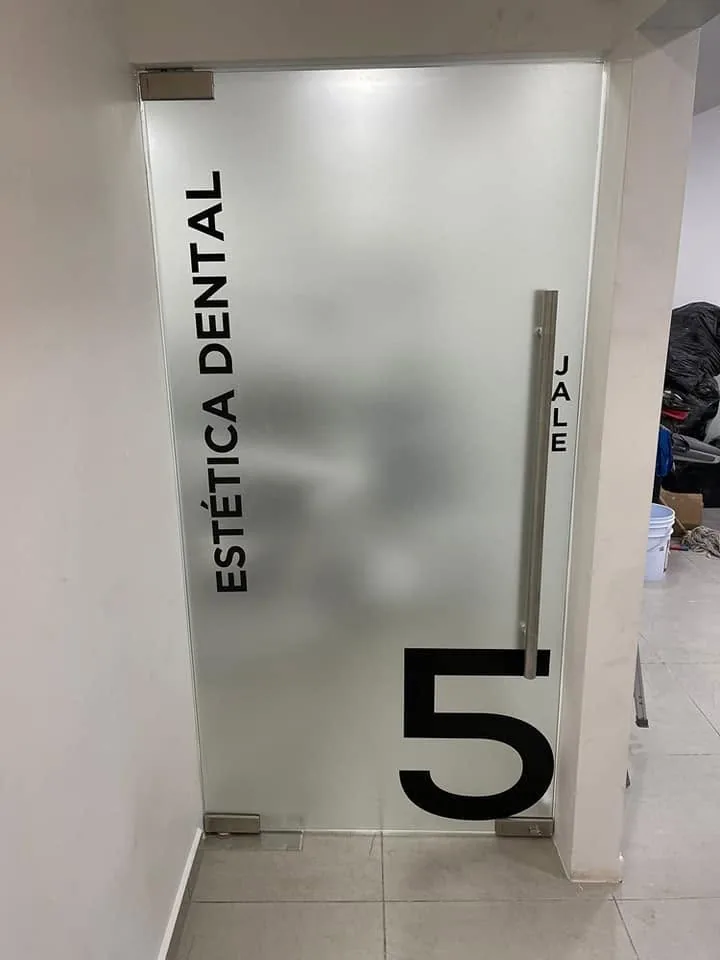 Puerta de cristal esmerilado con el texto Estética Dental y el número 5 en vinil de corte negro
