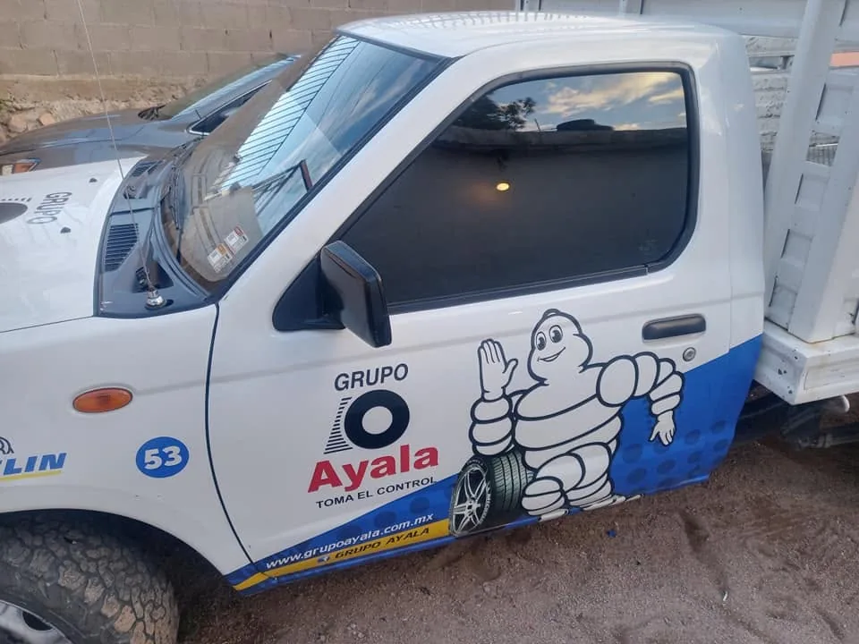 Camioneta blanca rotulada con el logotipo de Grupo Ayala y la mascota de Michelin