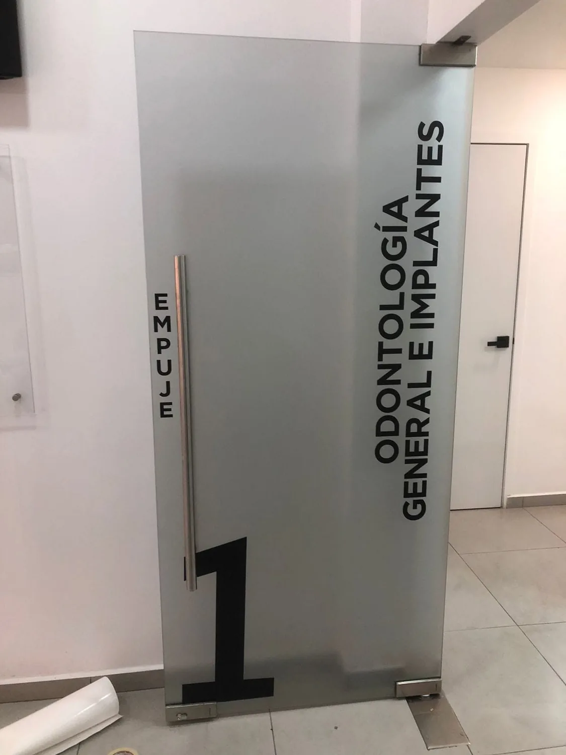 Puerta de cristal esmerilado con el texto Odontología General e Implantes en vinil de corte negro