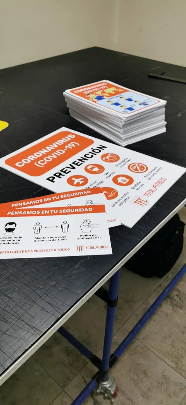 Letreros impresos de prevención de COVID-19 para Total Fitness apilados sobre la mesa